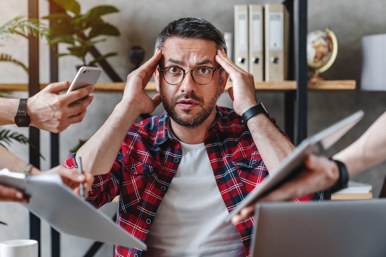 Businessman stressed about multiple task in an office with multiple gadget being presented.