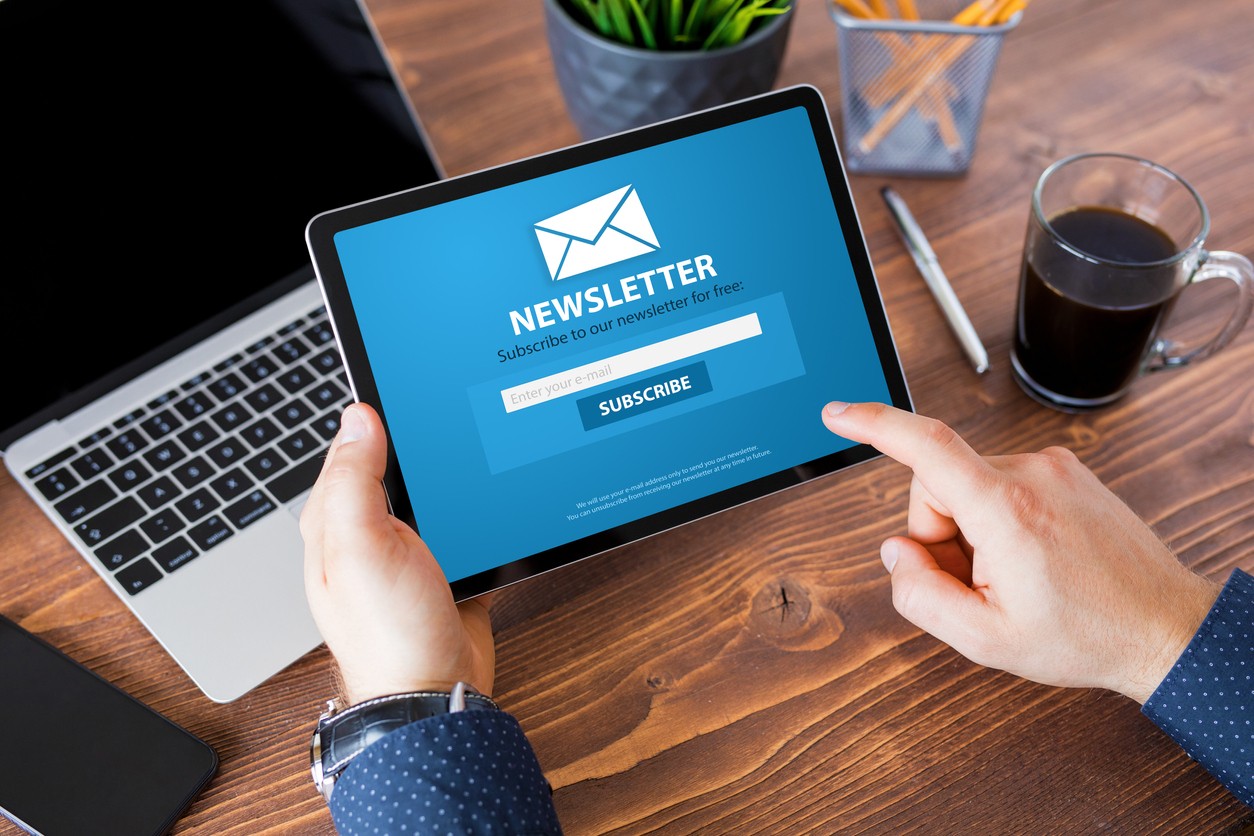 Man about to subscribe in a newsletter online with a cup of coffee, pen, smartphone and a laptop.